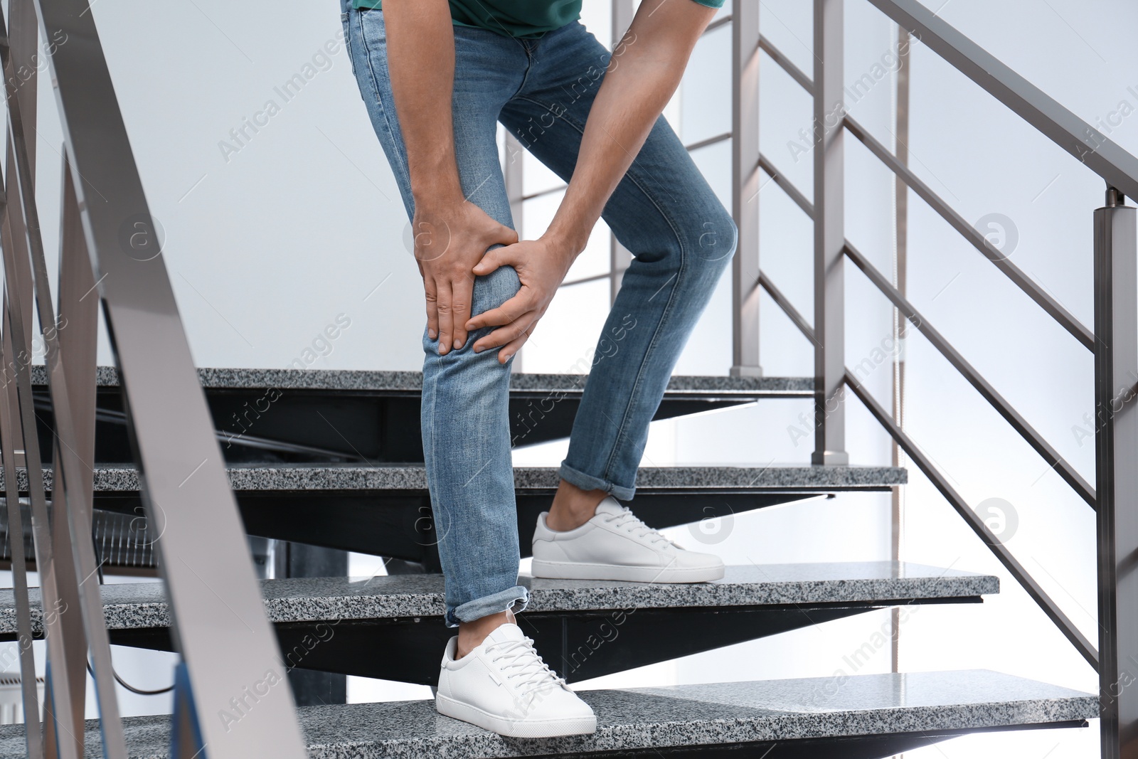 Photo of Man suffering from knee pain while going downstairs indoors, closeup. Health problems