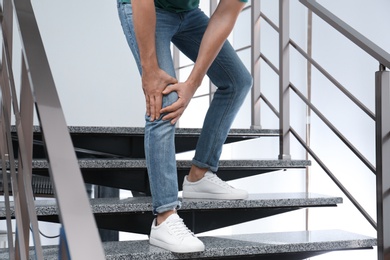 Man suffering from knee pain while going downstairs indoors, closeup. Health problems