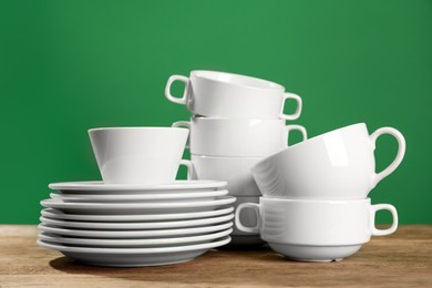 Photo of Set of clean dishware on wooden table against green background