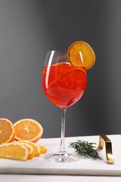 Glass of tasty Aperol spritz cocktail with orange slices and rosemary on white table against gray background