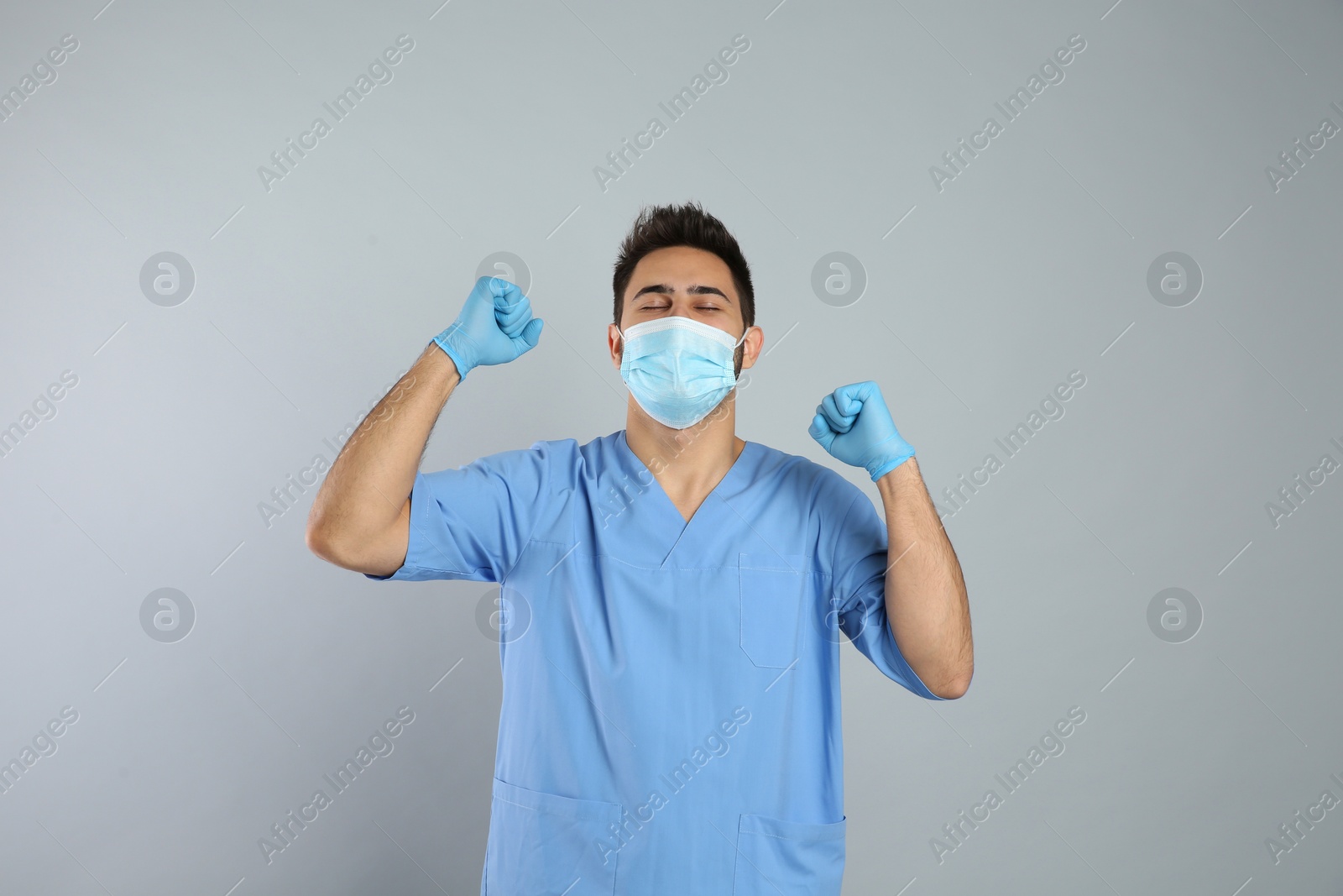 Photo of Emotional doctor with protective mask on light grey background. Strong immunity concept