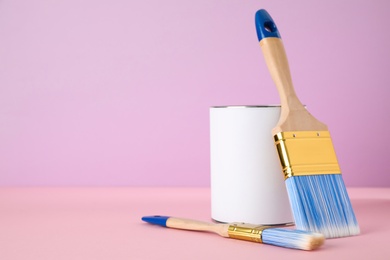 Photo of Blank can of paint with brushes on table against color background. Space for text
