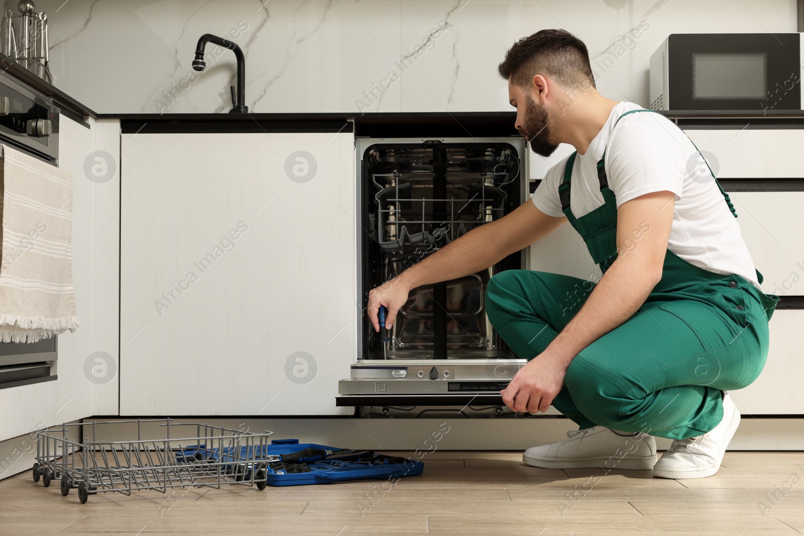 Photo of Serviceman repairing dishwasher door with screwdriver in kitchen