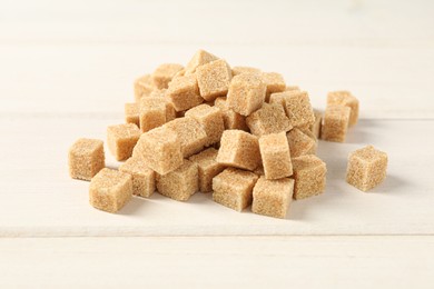 Photo of Heap of brown sugar cubes on white wooden table