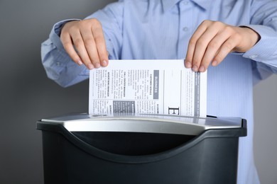 Photo of Woman destroying newspaper with shredder on grey background, closeup