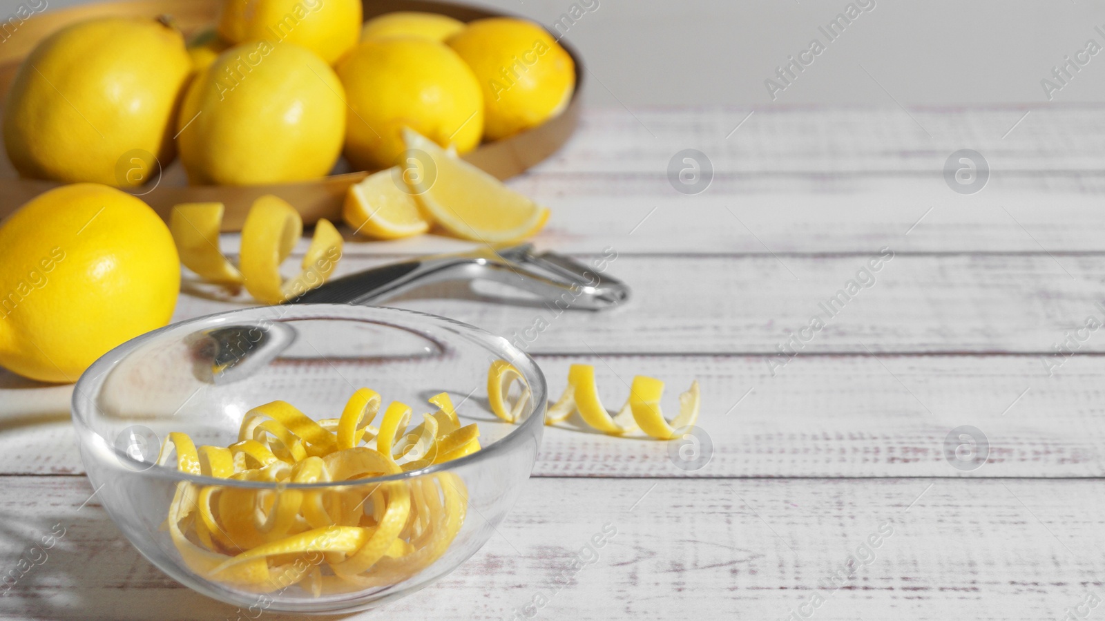 Photo of Bowl with peel pieces, fresh lemons and zester on white wooden table. Space for text