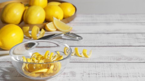 Bowl with peel pieces, fresh lemons and zester on white wooden table. Space for text