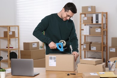 Photo of Seller taping parcel at workplace in office. Online store