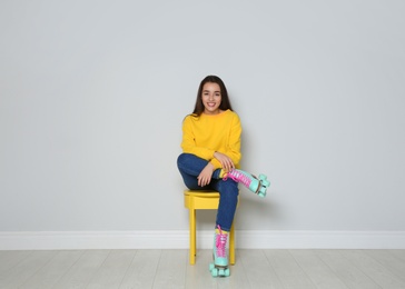 Photo of Young woman with roller skates sitting on chair near color wall