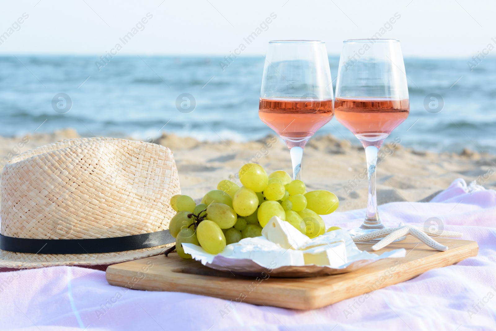 Photo of Glasses with rose wine and snacks for beach picnic on sandy seashore