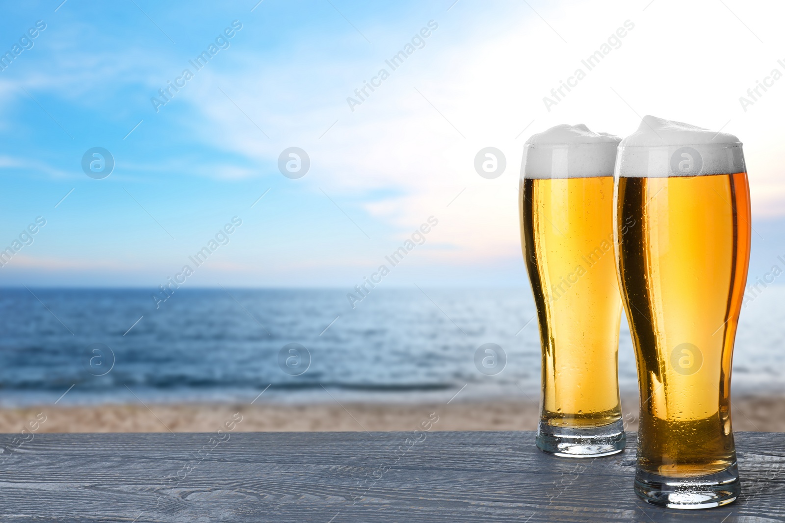 Image of Cold beer on wooden desk against blurred sea. Space for text