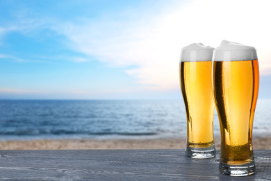 Image of Cold beer on wooden desk against blurred sea. Space for text