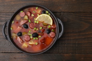 Meat solyanka soup with thin dry smoked sausages in bowl on wooden table, top view. Space for text