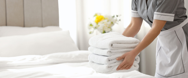 Image of Young chambermaid putting stack of fresh towels in bedroom, closeup view with space for text. Banner design