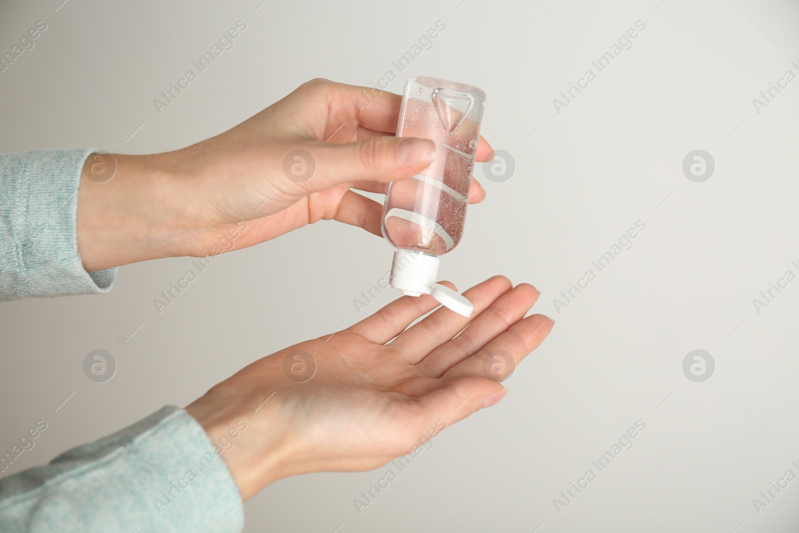 Photo of Woman applying antiseptic gel on light grey background, closeup