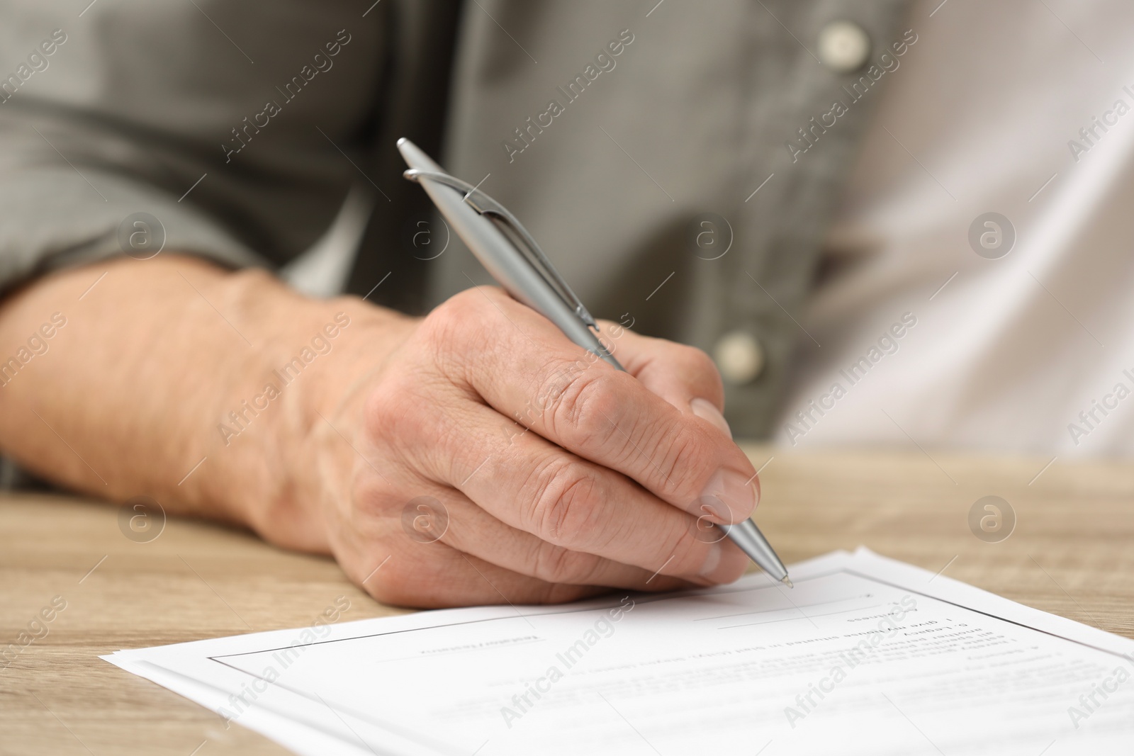 Photo of Senior man signing Last Will and Testament at wooden table, closeup