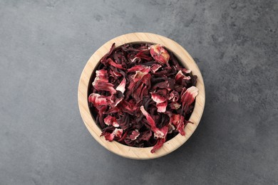Photo of Hibiscus tea. Wooden bowl with dried roselle calyces on grey table, top view