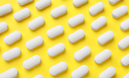 Photo of Vitamin pills on yellow background, flat lay