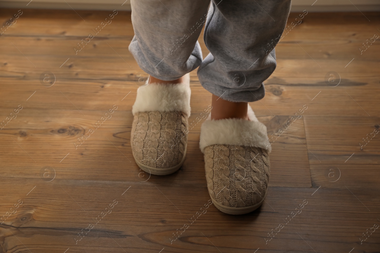 Photo of Woman wearing warm beige slippers on wooden floor, closeup