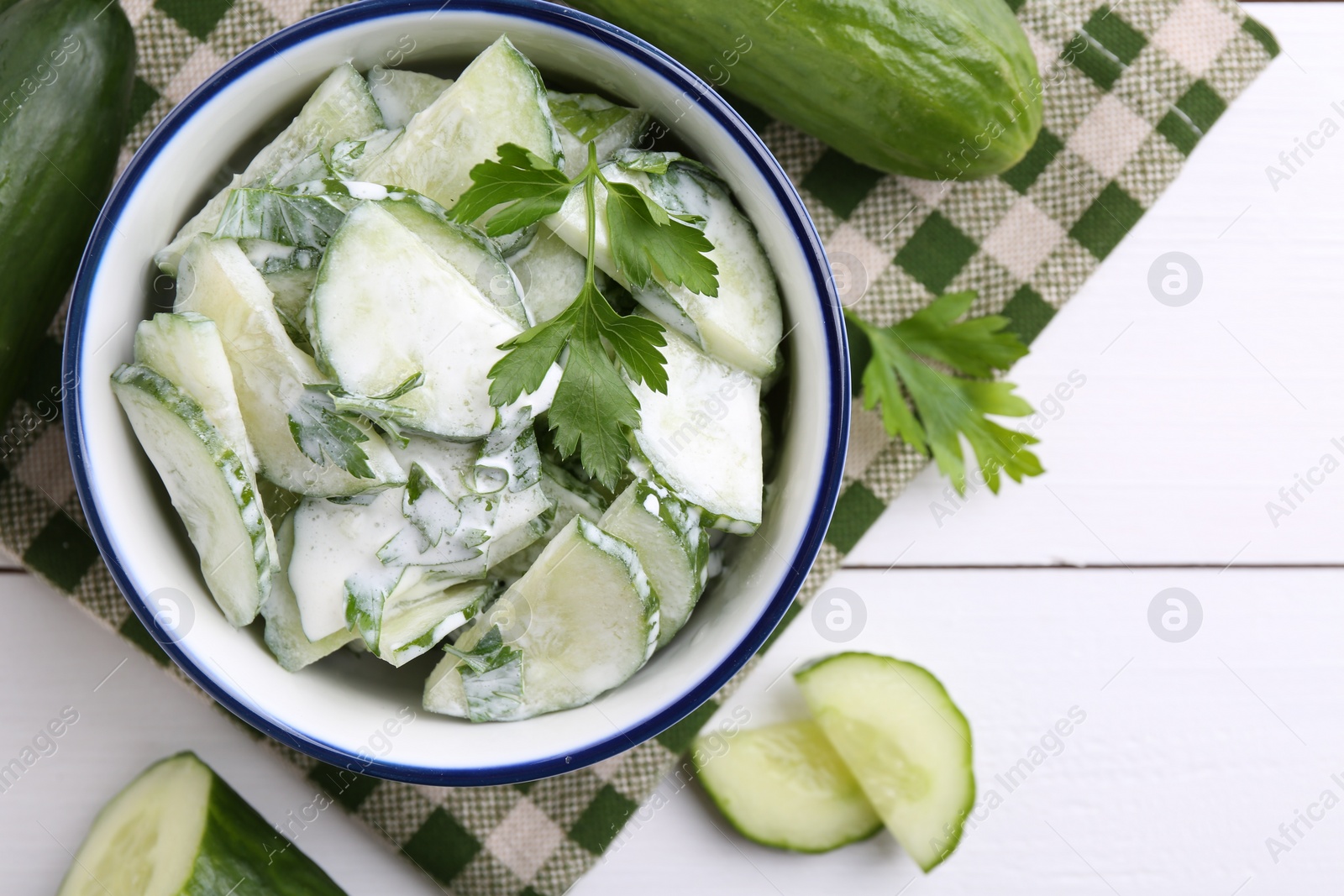 Photo of Delicious cucumber salad in bowl and ingredients on white wooden table, flat lay. Space for text