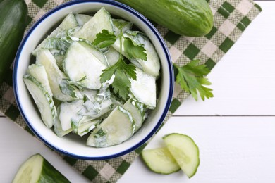 Delicious cucumber salad in bowl and ingredients on white wooden table, flat lay. Space for text