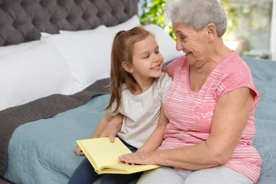 Cute girl and her grandmother reading book on bed at home