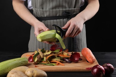 Photo of Woman peeling fresh zucchini at black wooden table, closeup