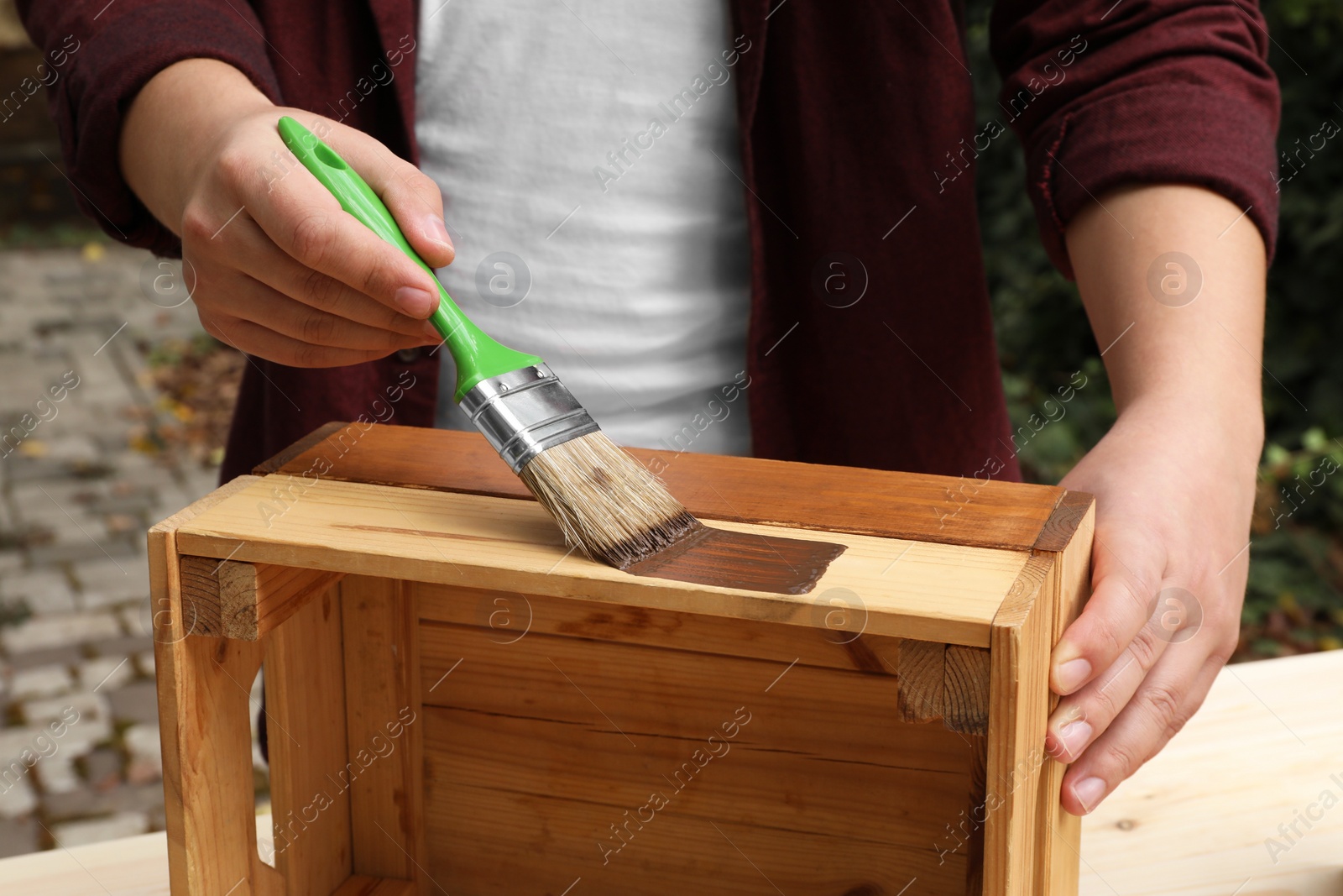 Photo of Man applying wood stain onto crate at table outdoors, closeup