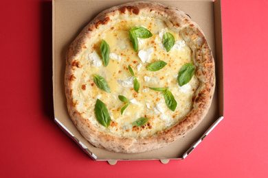 Photo of Delicious cheese pizza with basil in takeout box on red background, top view
