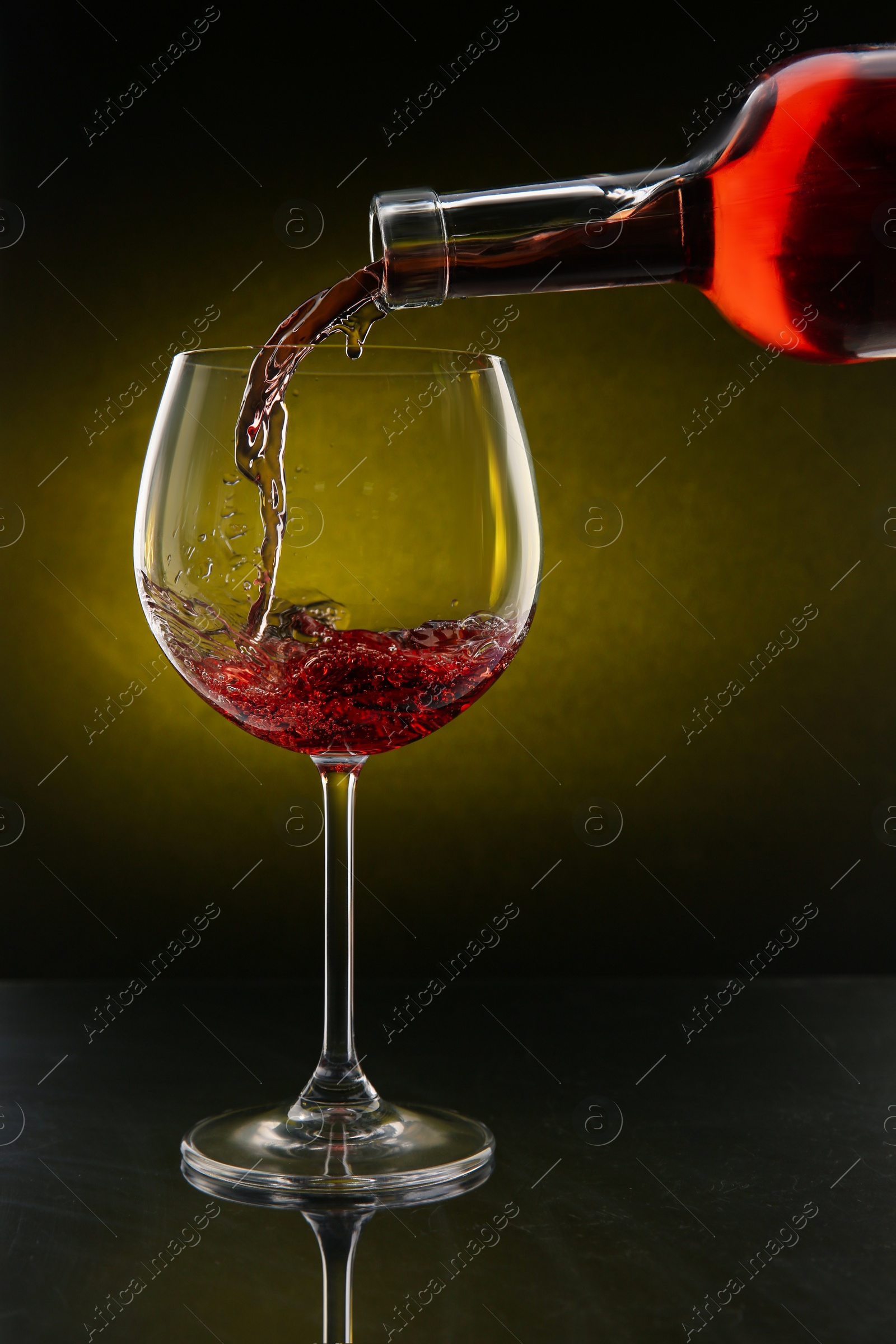 Photo of Pouring red wine from bottle into glass on color background