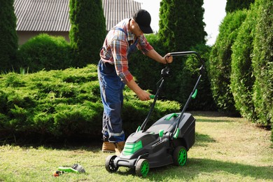 Photo of Young man fixing lawn mower in garden