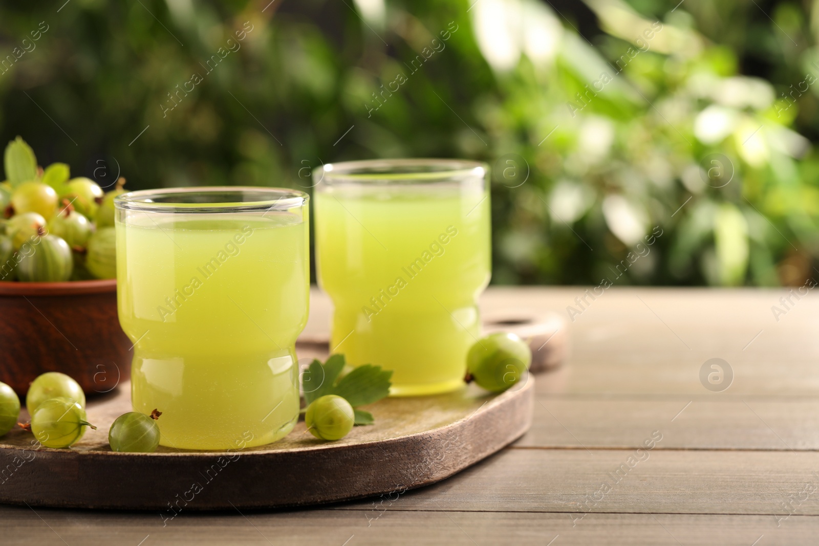 Photo of Tasty gooseberry juice and fresh berries on wooden table. Space for text