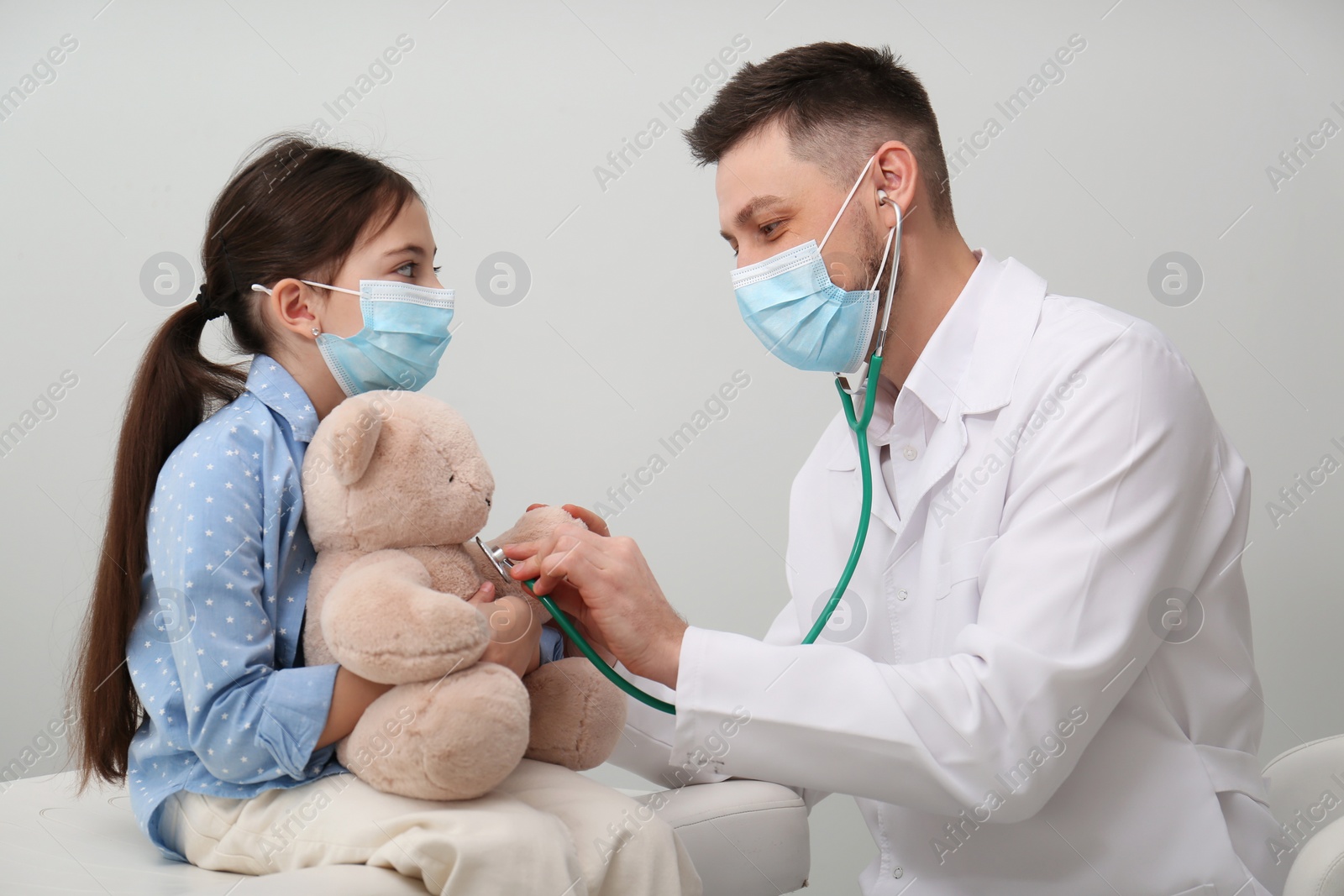 Photo of Pediatrician playing with little girl during visit in hospital. Doctor and patient wearing protective masks