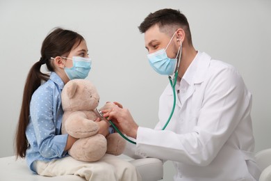 Pediatrician playing with little girl during visit in hospital. Doctor and patient wearing protective masks