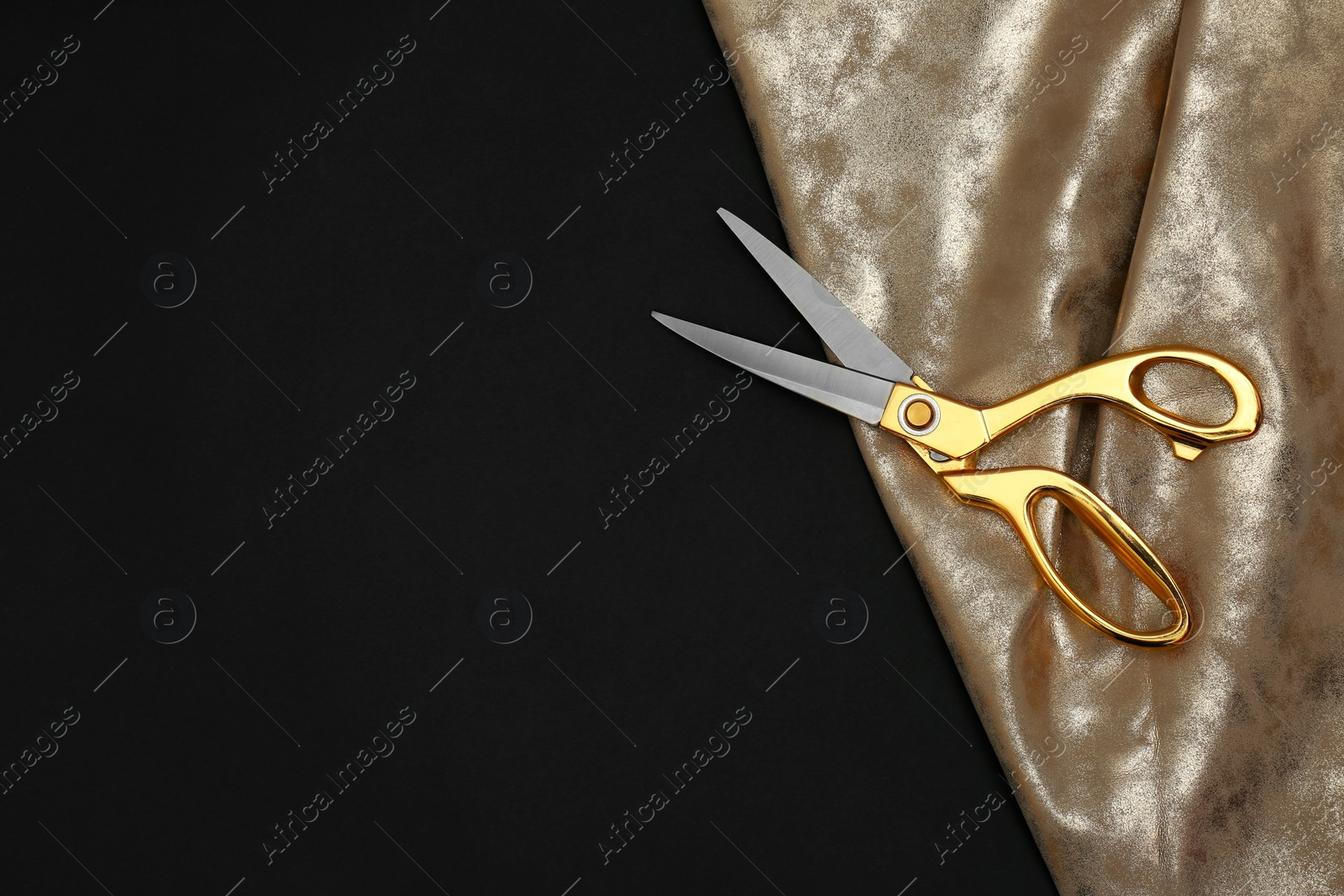 Photo of Gold tailor scissors and fabric on black background, top view with space for text