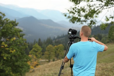 Photo of Photographer taking video with modern camera on tripod in mountains