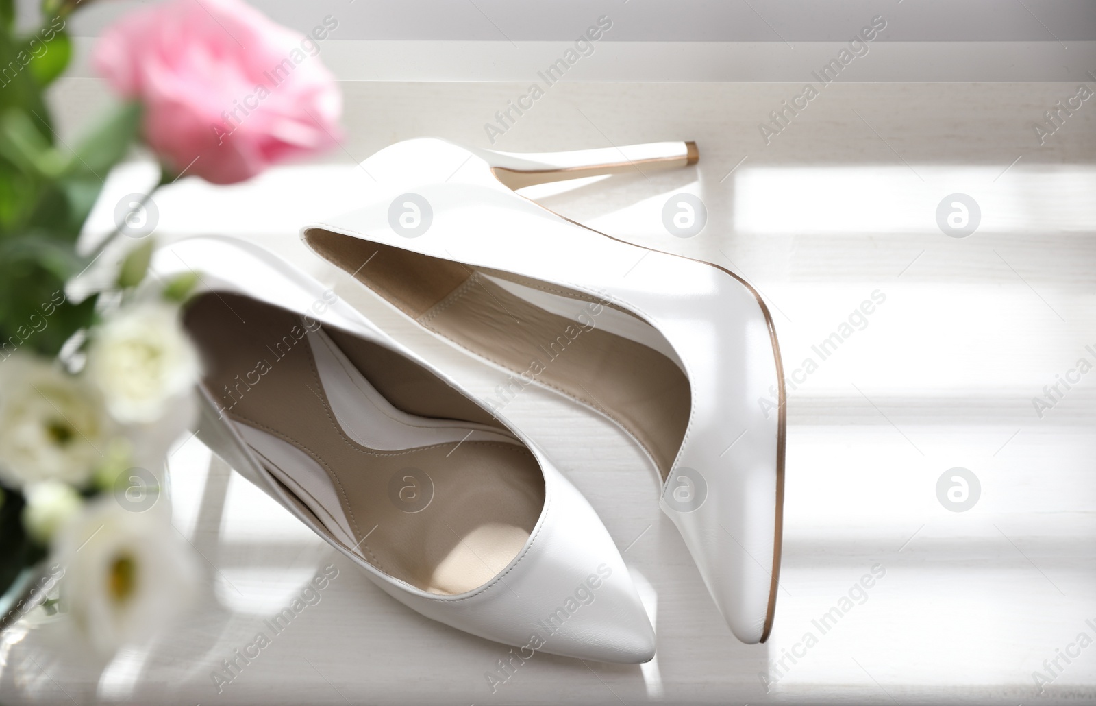 Photo of Pair of white high heel shoes and wedding bouquet on windowsill, top view