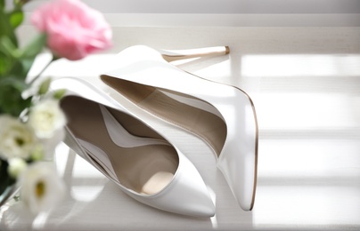 Photo of Pair of white high heel shoes and wedding bouquet on windowsill, top view