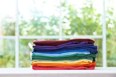 Photo of Stack of bright folded clothes on table against blurred background. Space for text