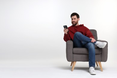 Photo of Happy man with smartphone sitting on armchair against white background. Space for text