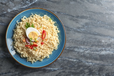 Plate of tasty noodles with egg and vegetables on marble background, top view. Space for text