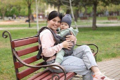 Mother holding her child in sling (baby carrier) on bench in park