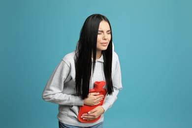 Photo of Woman using hot water bottle to relieve abdominal pain on light blue background