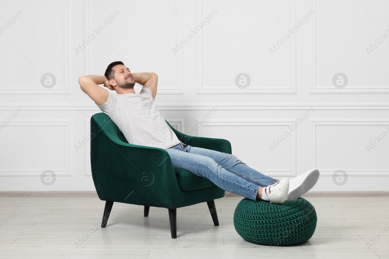 Photo of Happy man sitting in armchair near white wall indoors