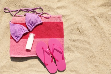 Beach towel with slippers, sunscreen and swimsuit on sand, flat lay. Space for text