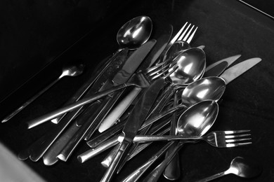 Photo of Silver spoons, forks and knives after washing on black table, above view