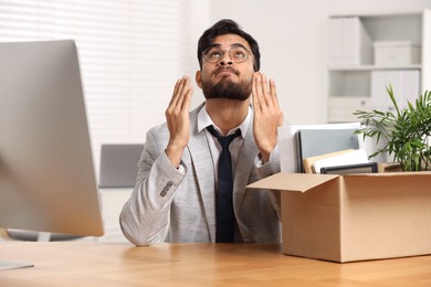 Photo of Unemployment problem. Frustrated man with box of personal belongings at desk in office