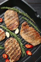 Photo of Grill pan with delicious pork steaks, garlic, chili pepper and rosemary on table, top view