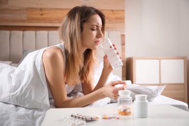 Photo of Woman taking medicine for hangover in bed at home