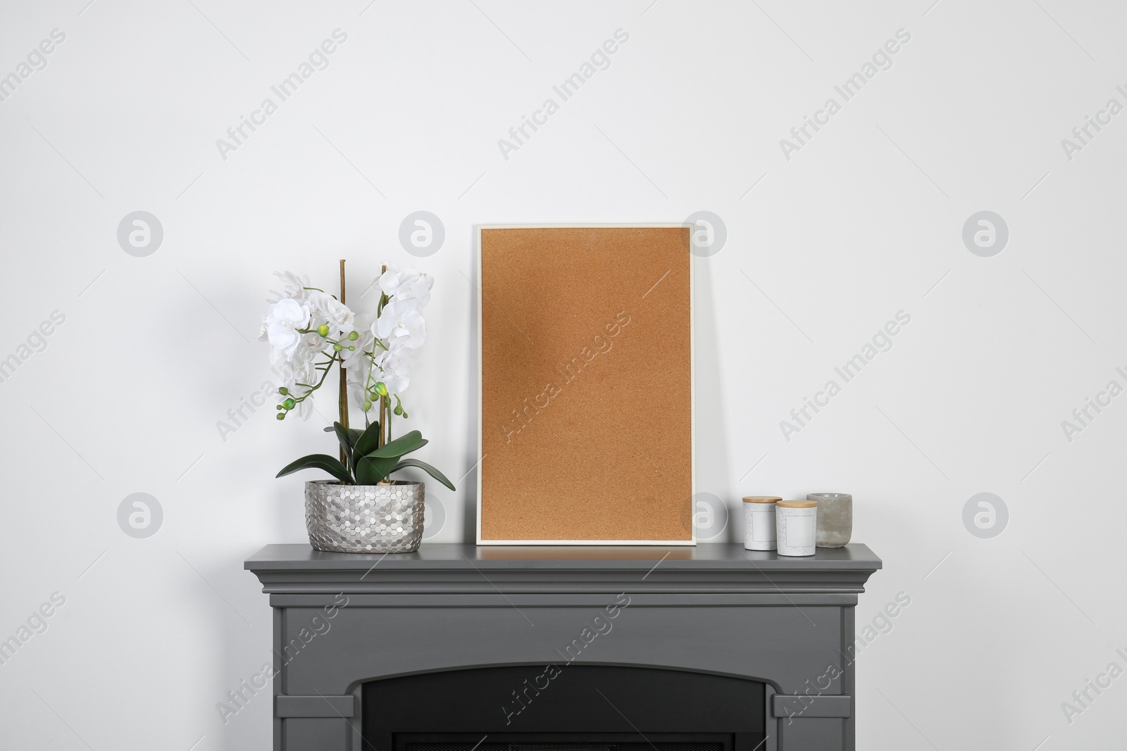 Photo of Picture frame, candles and orchid on fireplace near white wall indoors. Interior element